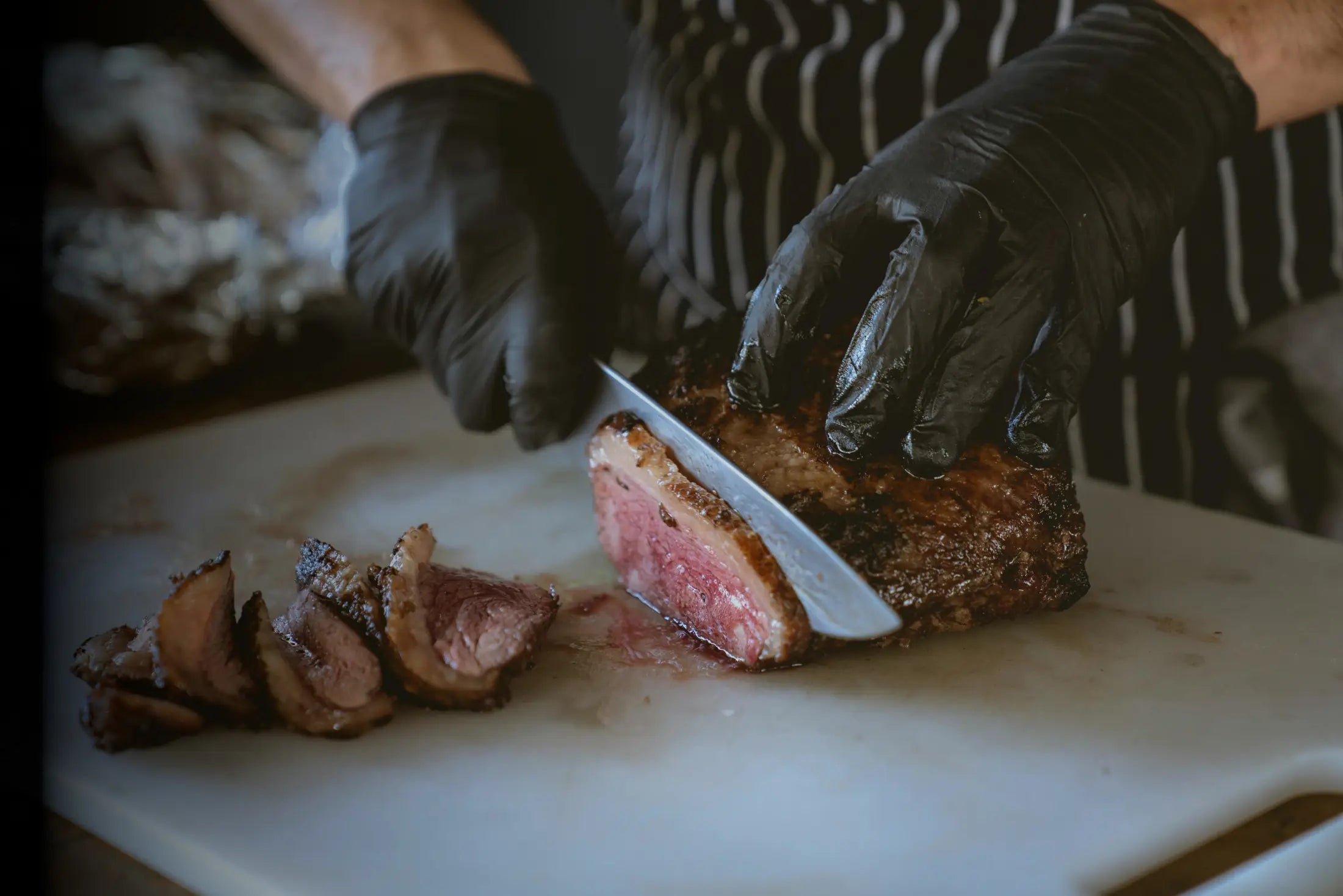 Chef Cutting Steak with a Damascus Steel knife on a white  cutting board with black gloves on. | Boulder & Blade